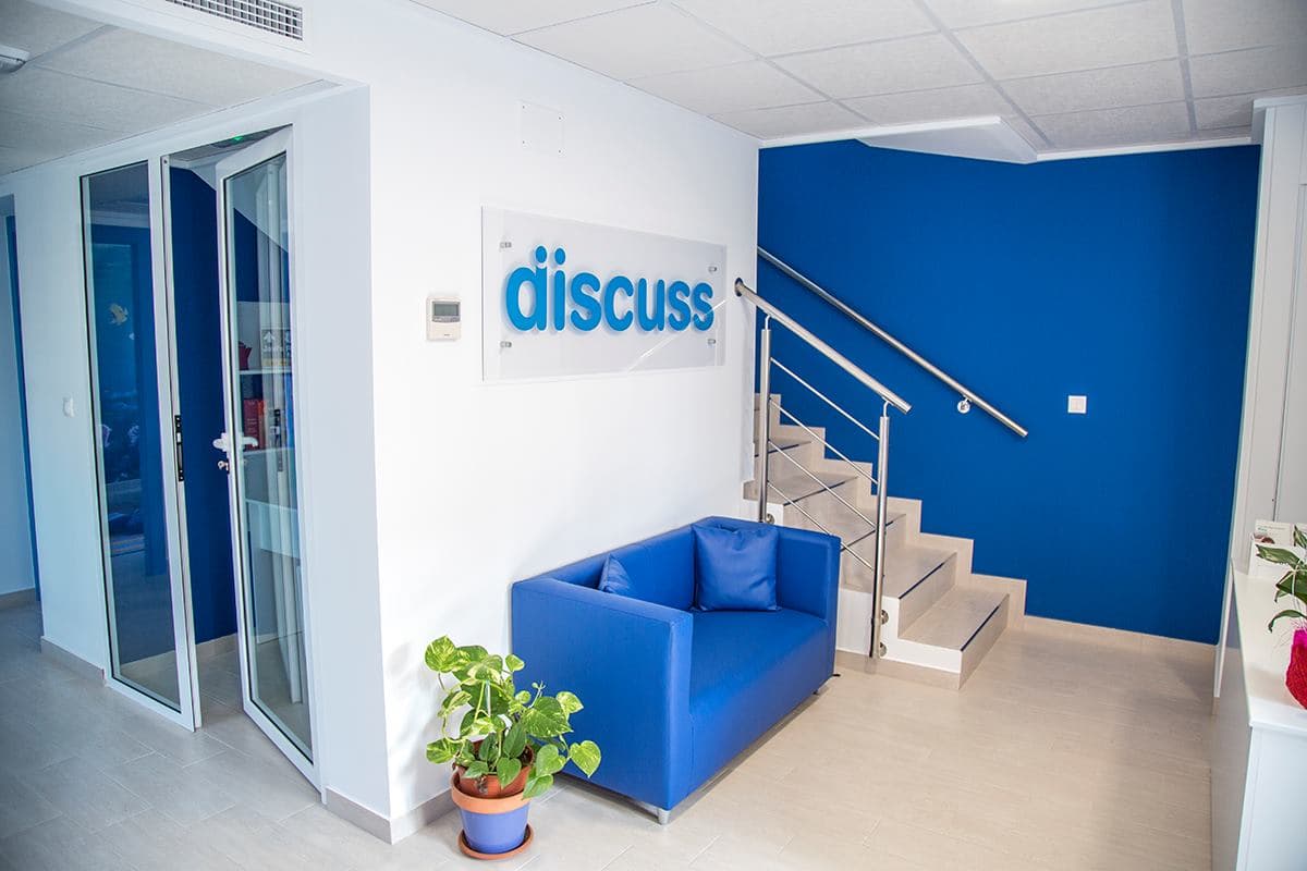 Recepción de la academia Discuss Idiomas con logo, sofá de espera y acceso a plantas superiores